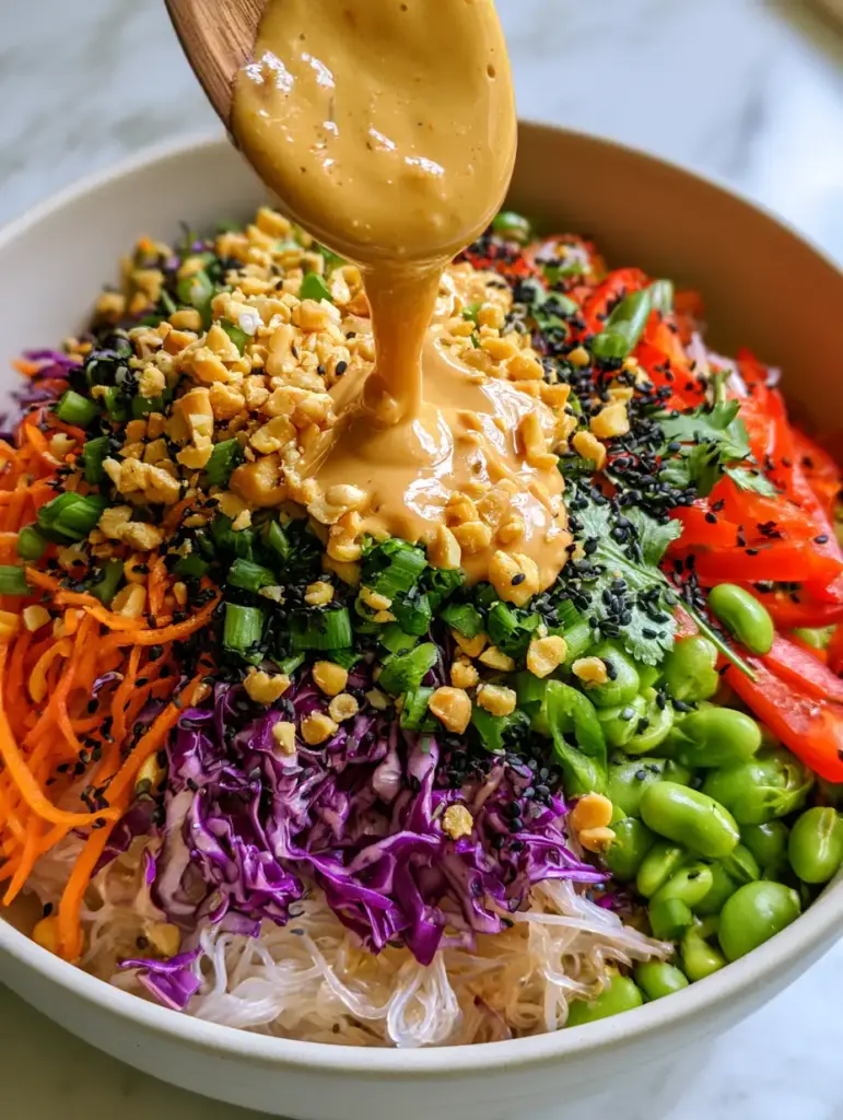 No Cook Noodle Salad with Creamy Peanut Dressing 1 Close-up of creamy tan peanut dressing being drizzled from a wooden spoon onto a No Cook Noodle Salad.